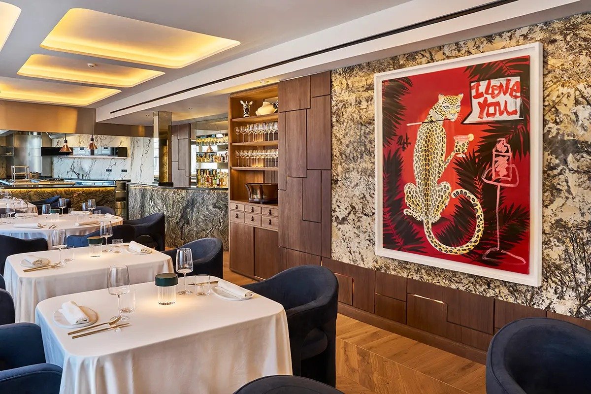 A dining room with white-clothed tables, dark blue chairs and a large leopard artwork on a marble wall.