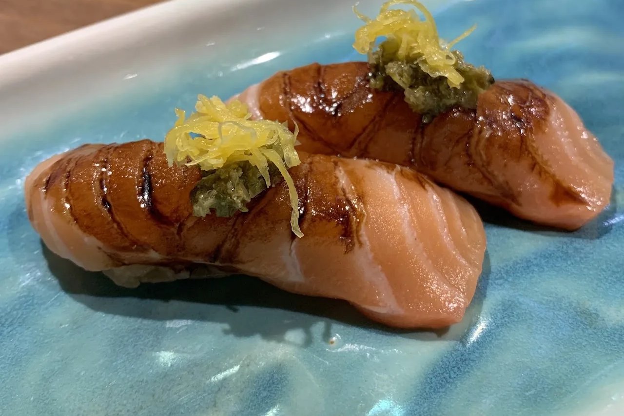 Two pieces of flame-seared salmon nigiri topped with grated yuzu zest on a pale blue plate