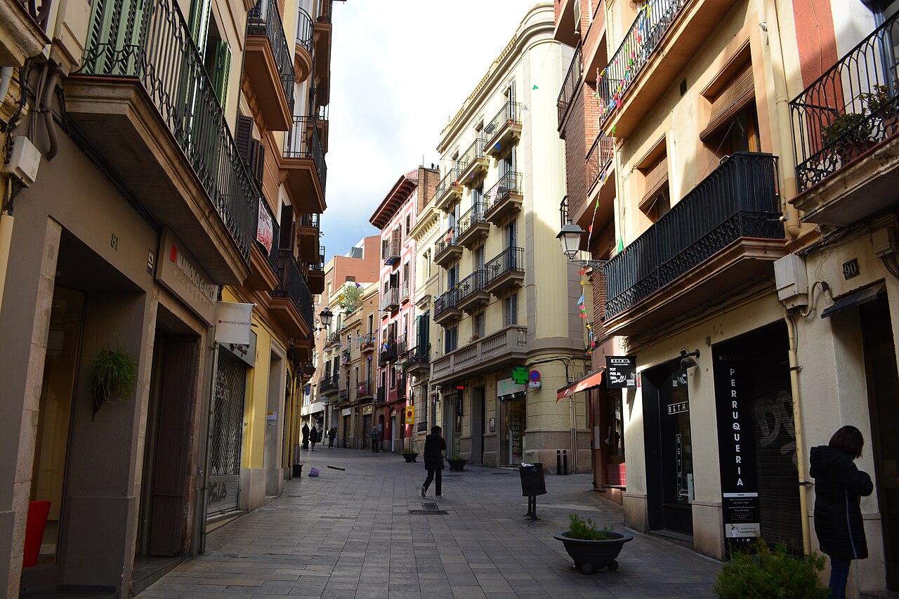 Looking down the pedestrian Carrer Major de Sarrià in Barcelona, lined with balconied buildings and shopfronts (illustrative, the shop itself is not shown)