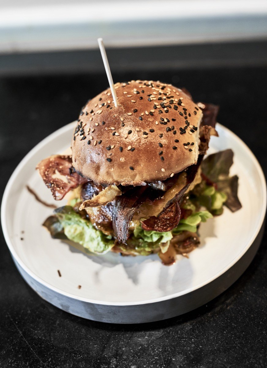 A gourmet burger with bacon and salad leaves on a plate at Badal Corner, Palma
