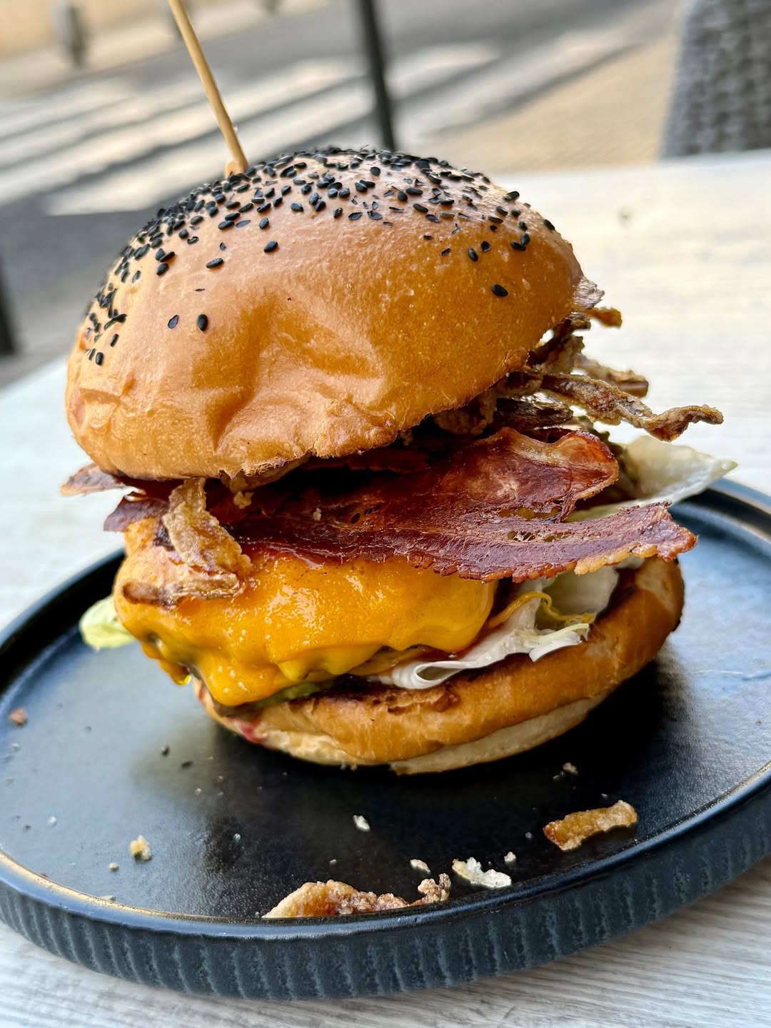 A cheeseburger with bacon on a black plate at Badal Corner