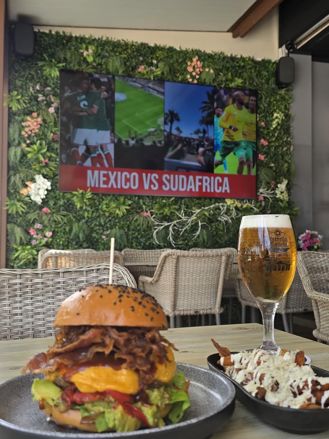 A burger with sides and a beer on a table at Badal Corner