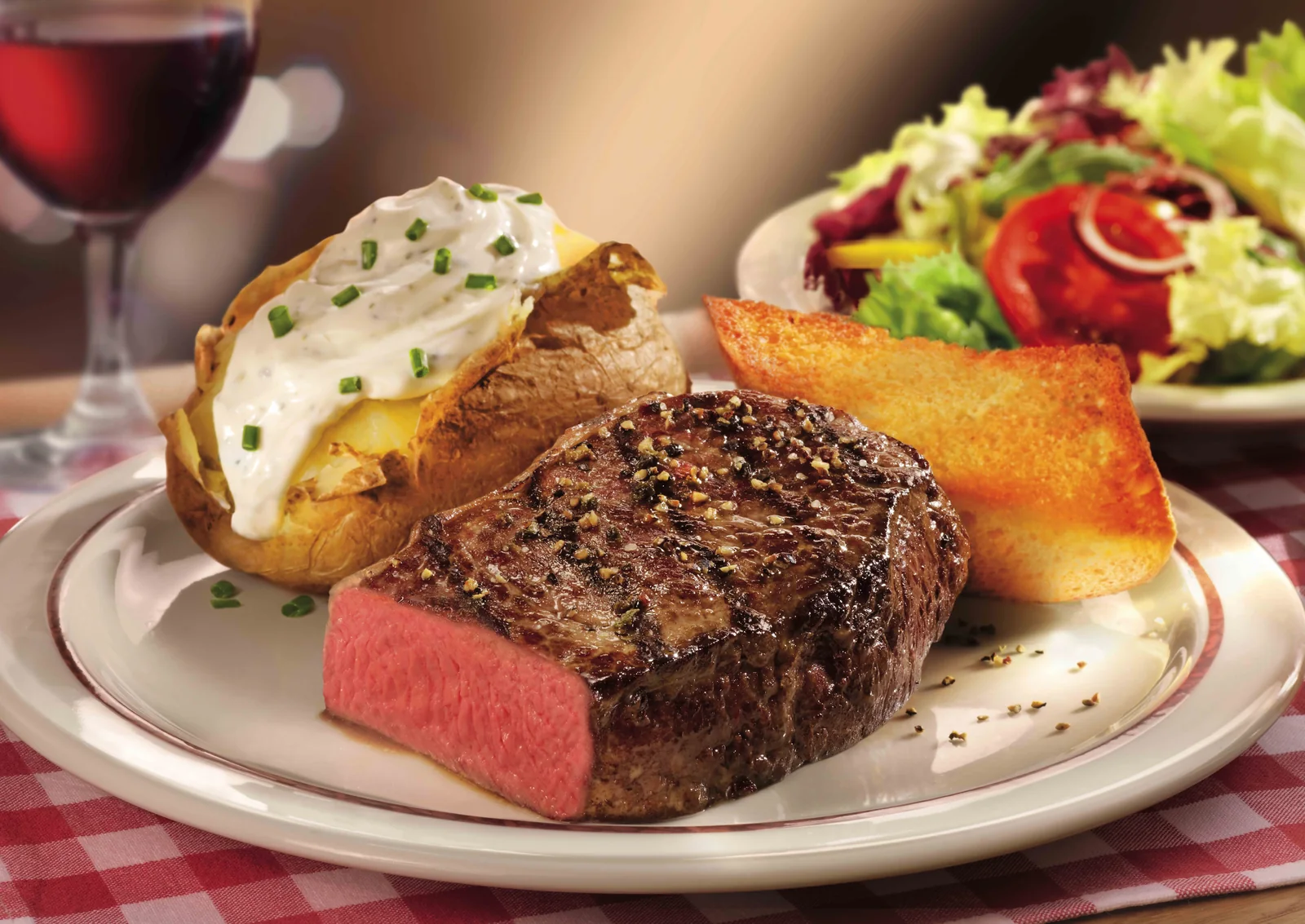 Sliced steak plated with baked potato, salad and red wine