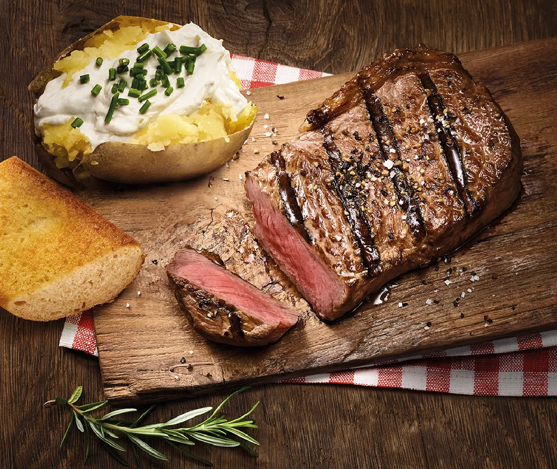 Sliced striploin steak on a board with toasted bread