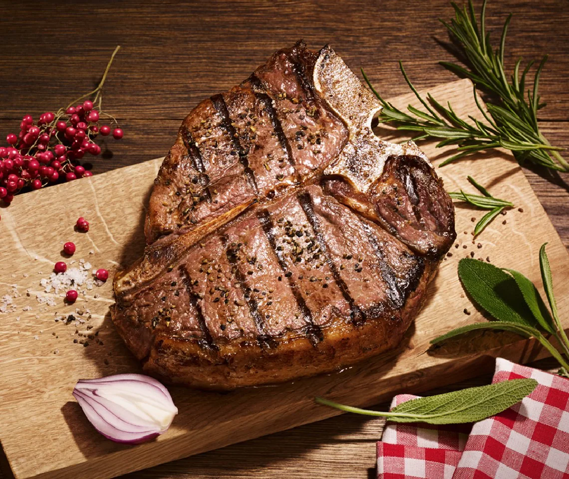 Grilled T-bone steak on a wooden board with herbs