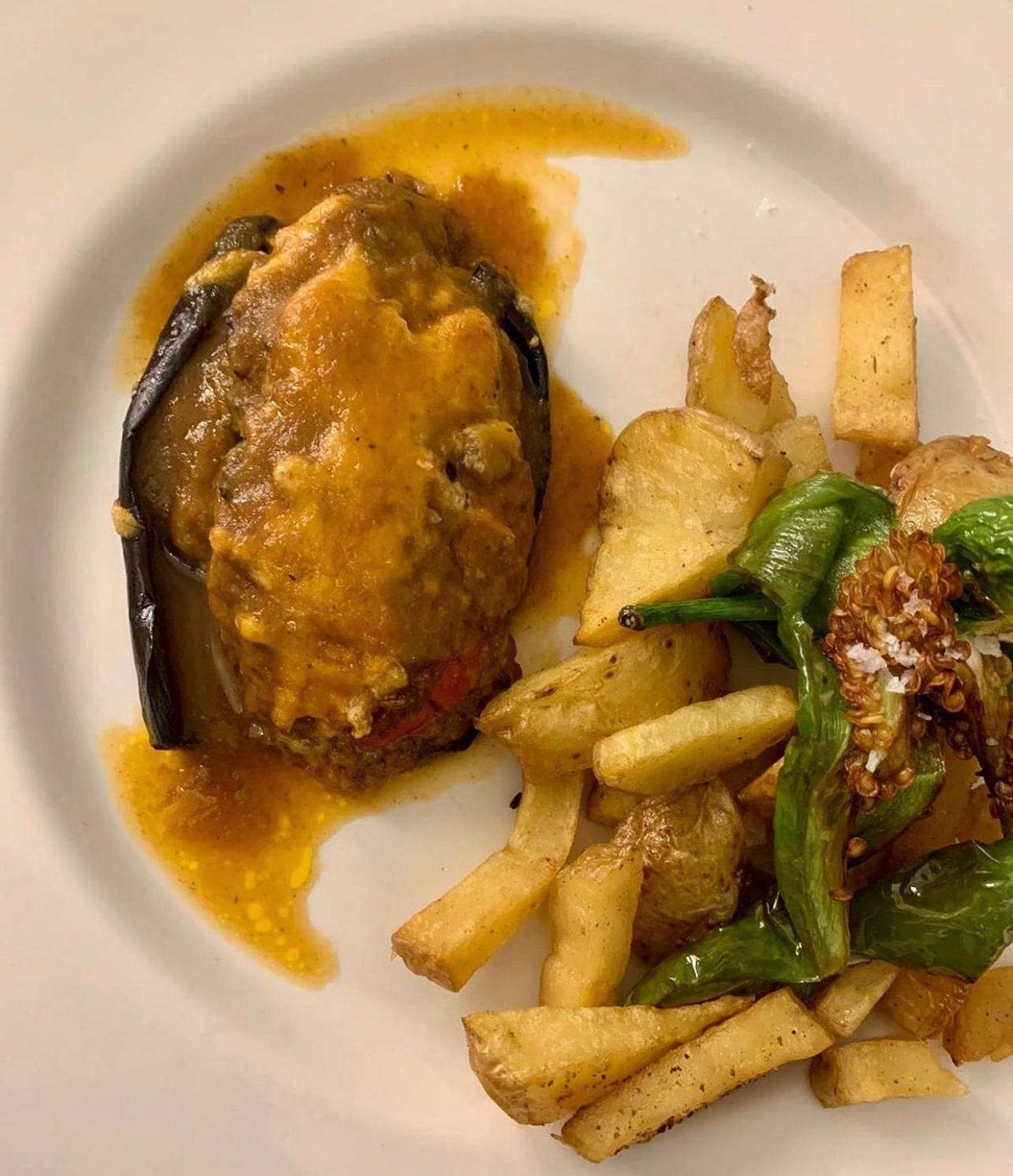 Stuffed eggplant in sauce beside fries and green peppers