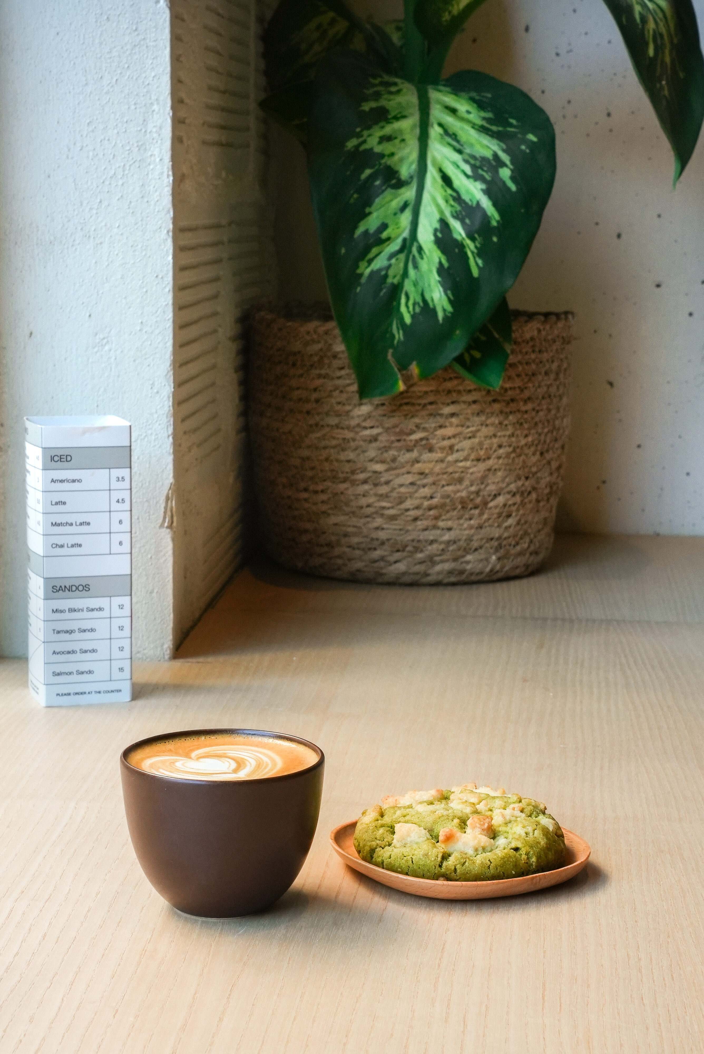 Latte with heart latte art beside a matcha white chocolate cookie