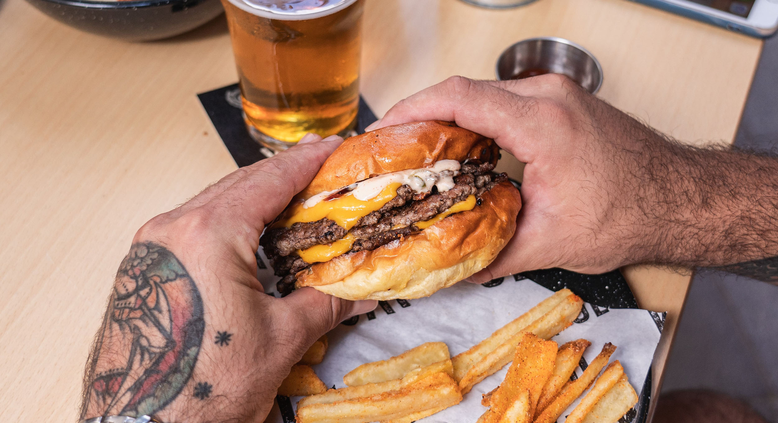 A cheeseburger held in hand over a basket of fries at Klüg Burgers, Palma