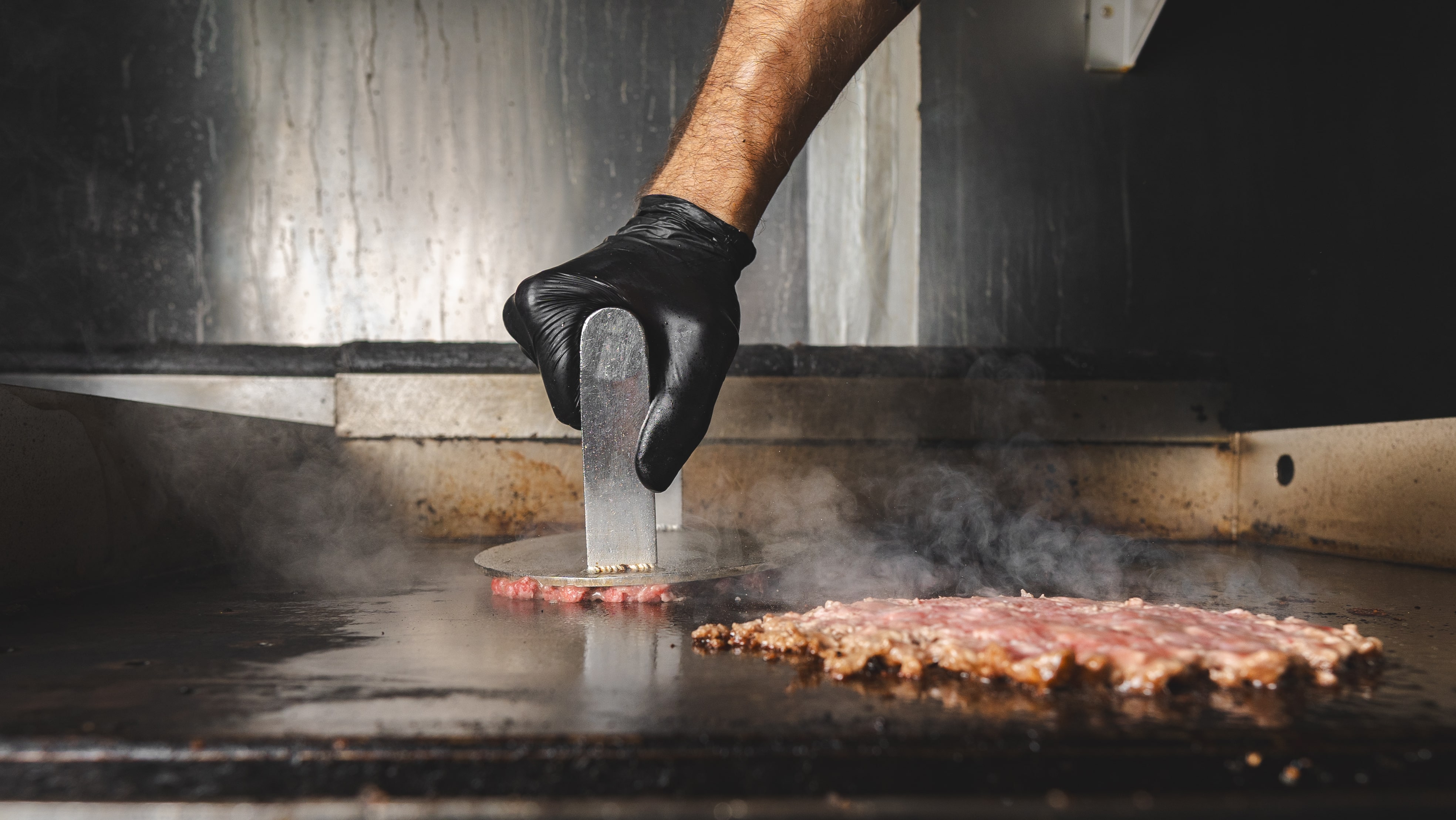 Smash patties searing on the flat-top griddle at Klüg Burgers