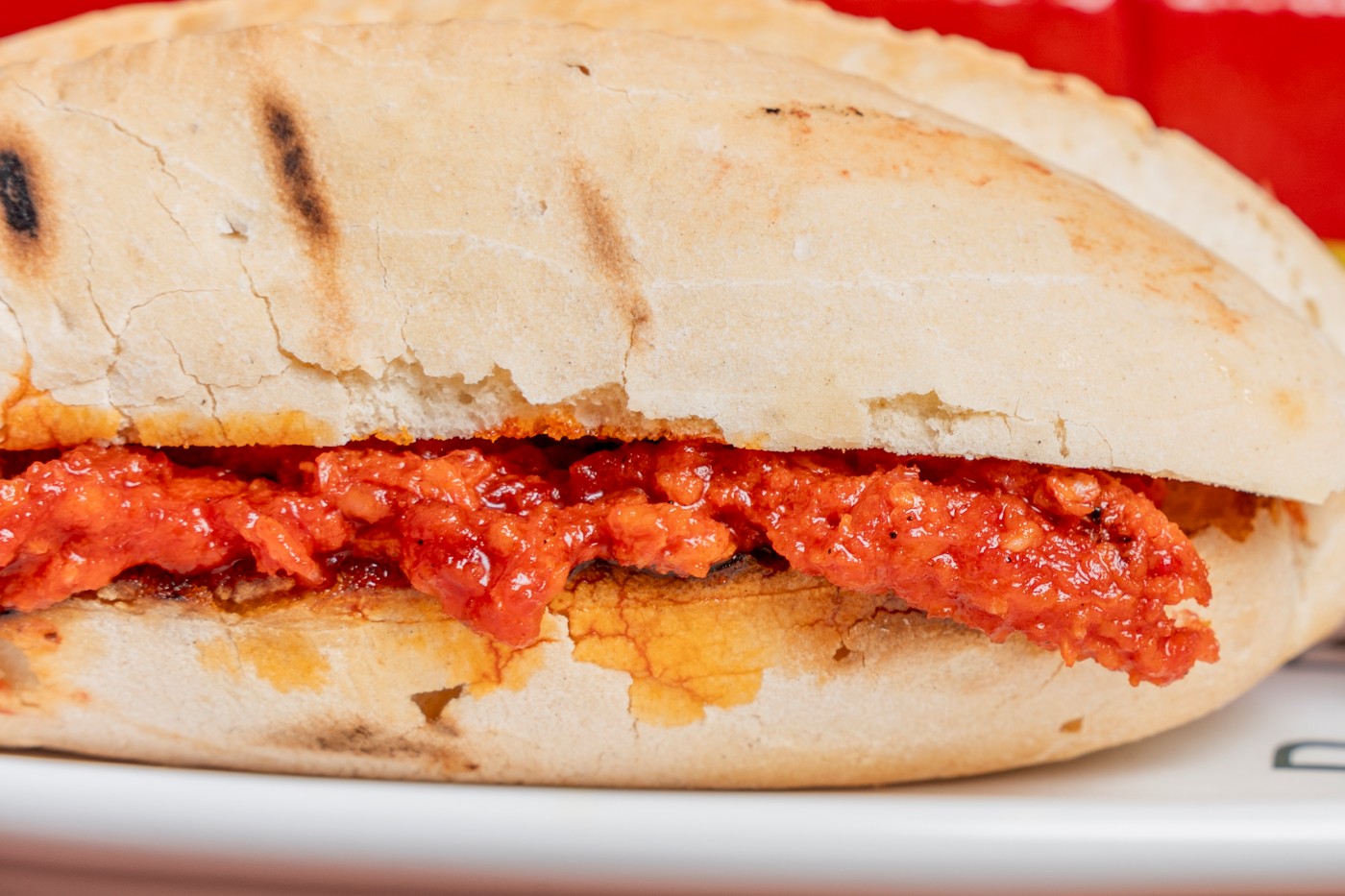A close-up of a grilled llonguet filled with red sobrassada spread on toasted bread.
