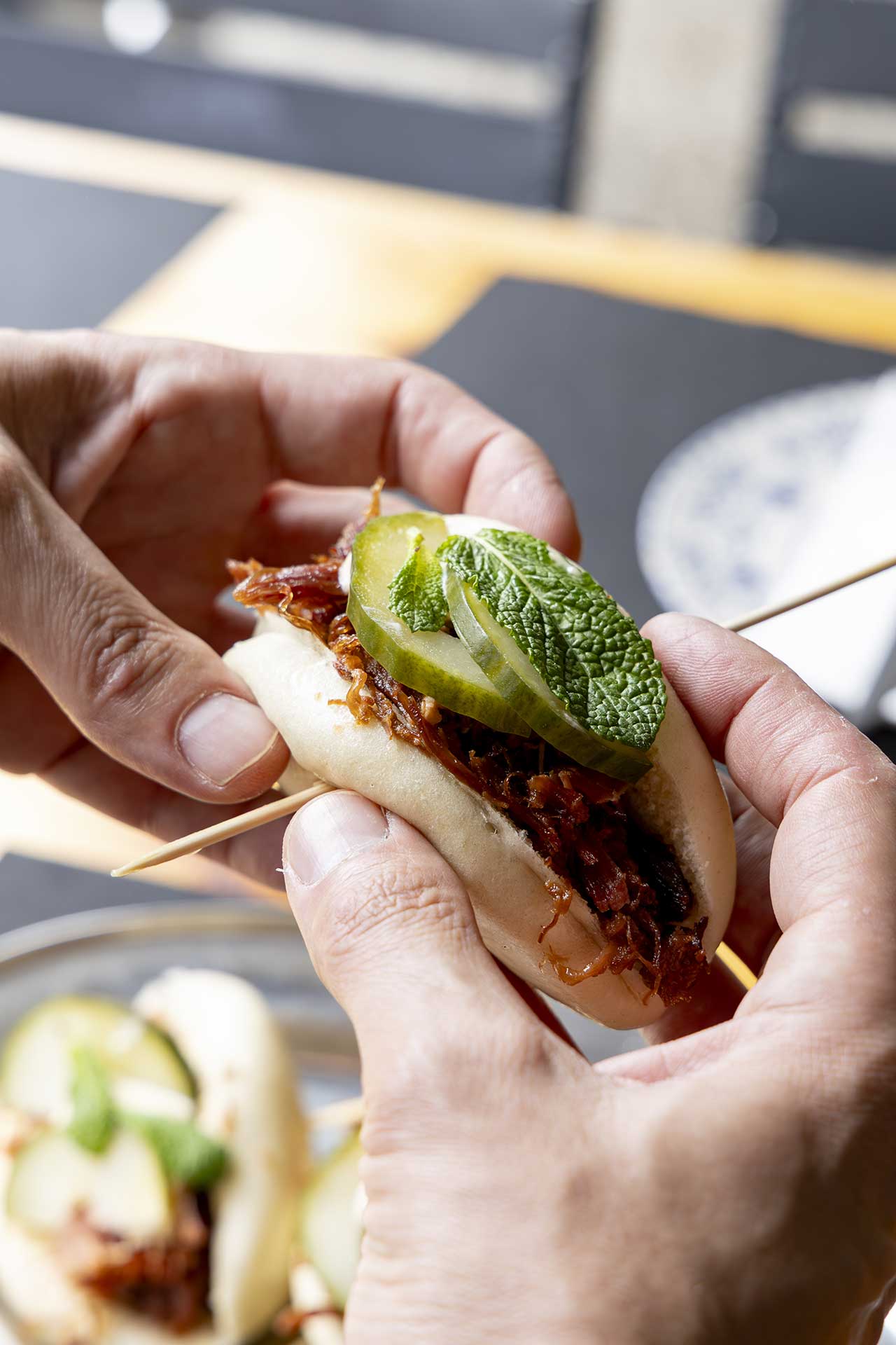 Hand holding a bao bun with pickle and mint