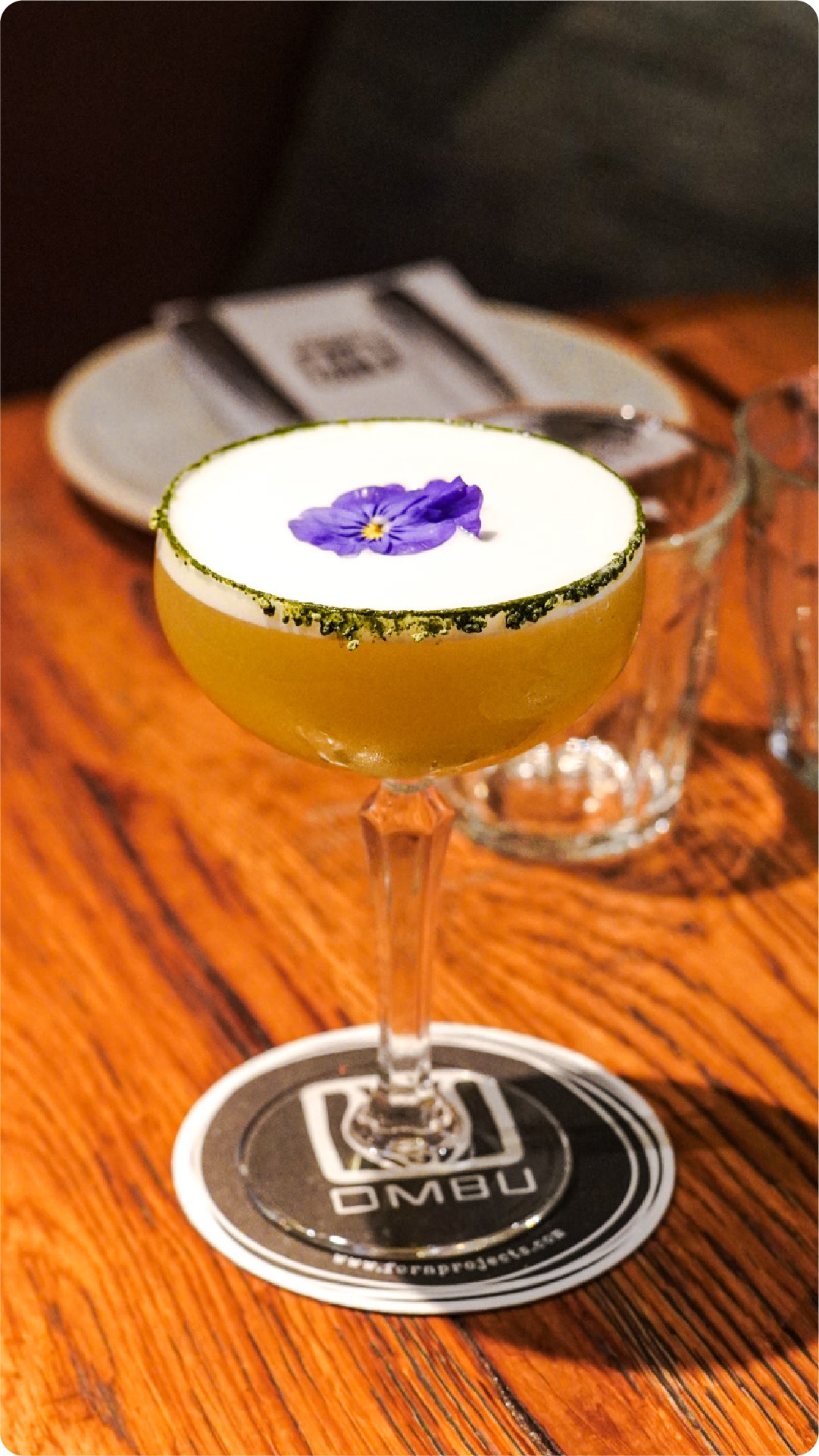 Cocktail with a pansy garnish on an OMBU branded coaster