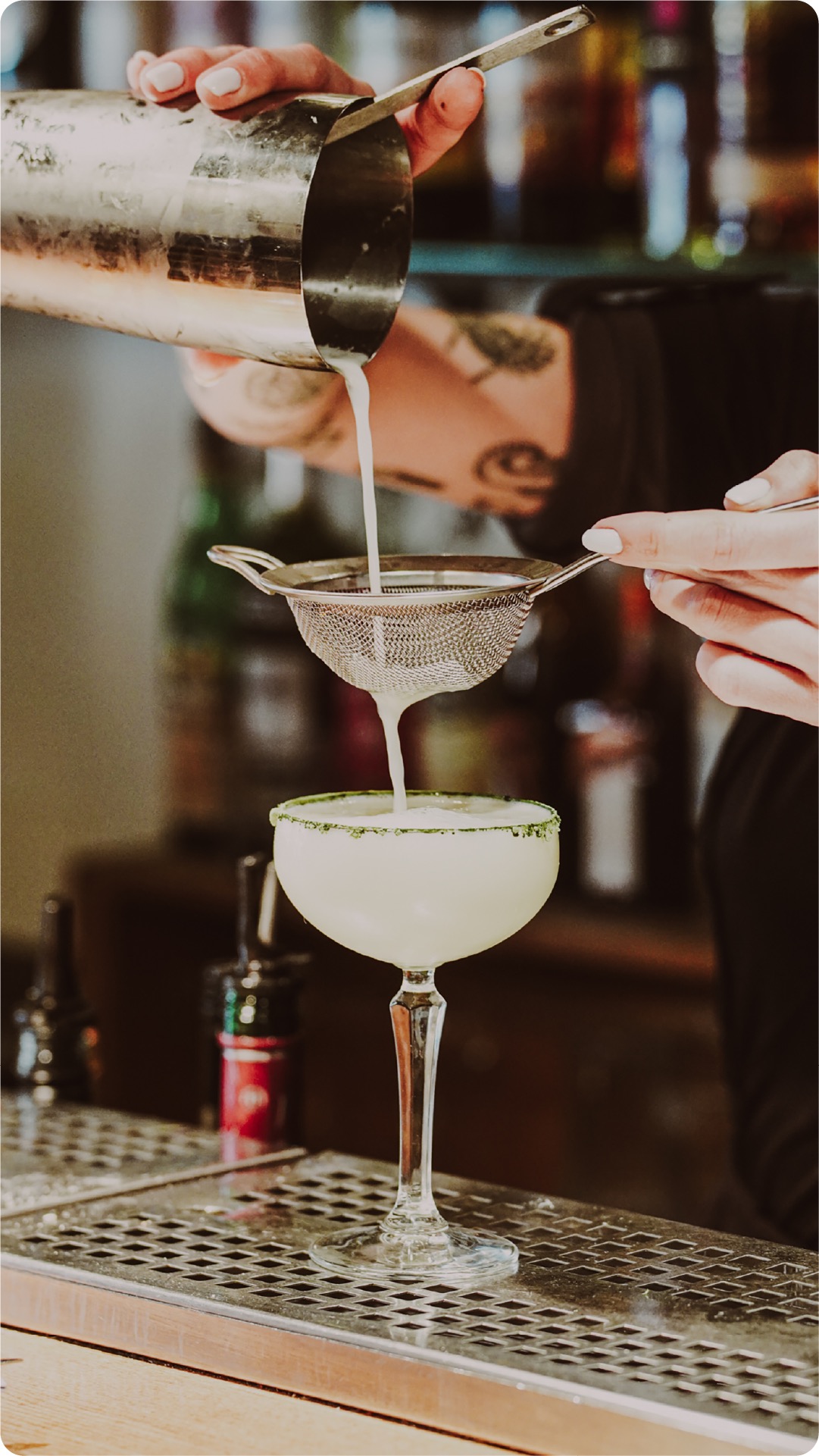Bartender straining a cocktail into a coupe glass at the bar