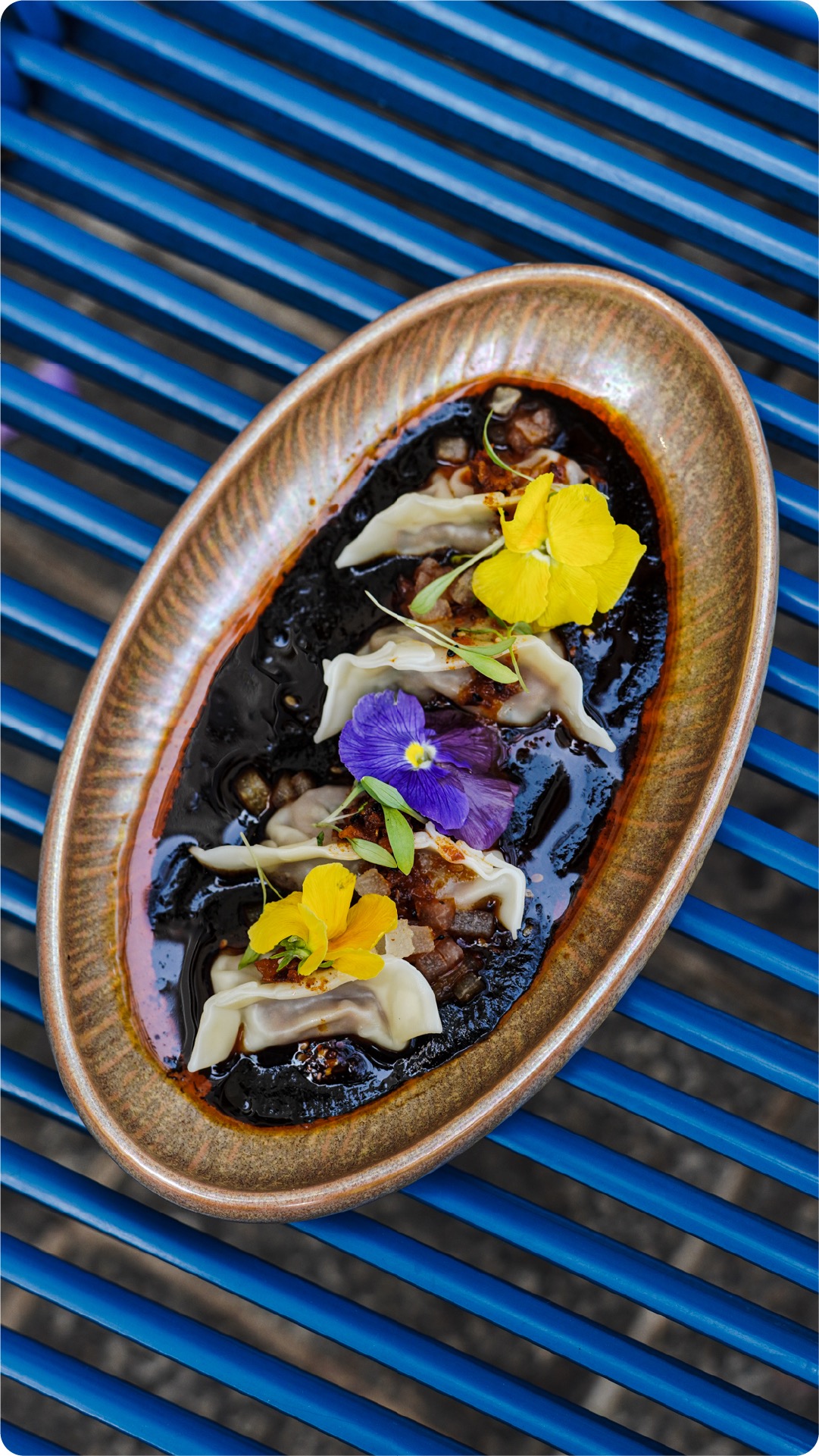 Peking duck gyozas in black garlic hoisin sauce with edible flowers