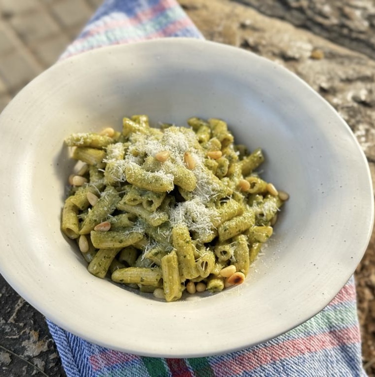 Bowl of pesto pasta topped with pine nuts and grated cheese